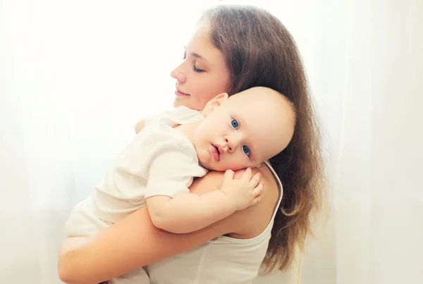 Portrait of loving mother hugging her baby over white window — Stock Photo, Image