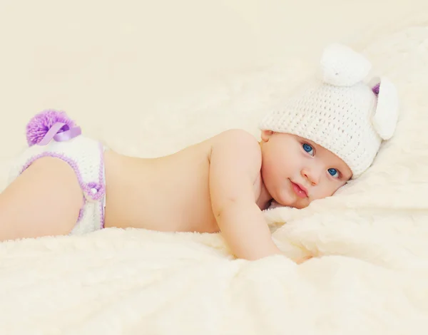 Dulce bebé en sombrero de punto con orejas de conejo acostado en la cama —  Fotos de Stock