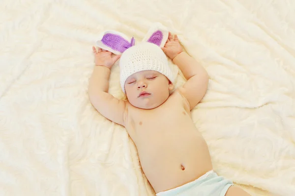 Dulce bebé en sombrero de punto con orejas de conejo dormir acostado en la cama —  Fotos de Stock