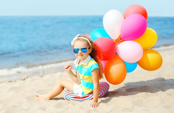 Niño sentado en la playa con globos de colores cerca del mar verano da —  Fotos de Stock