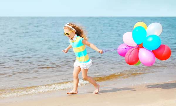 Criança sorridente feliz brincando na praia correndo com balão colorido — Fotografia de Stock