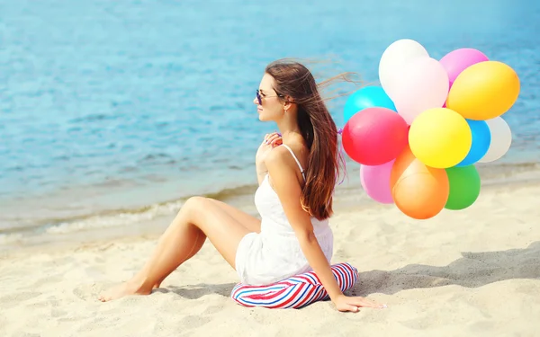 Felice giovane donna con palloncini colorati seduto sulla spiaggia vicino s — Foto Stock