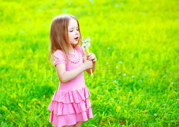 Dandelions çiçekler bahar güneşli bes üfleyen küçük kız çocuk — Stok fotoğraf