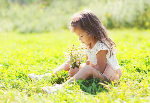 Kleines Mädchen sitzt mit einem Strauß Kamillenblüten auf — Stockfoto