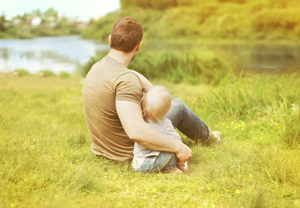 Счастливый отец и сын отдыхают, сидя вместе на траве летом — стоковое фото
