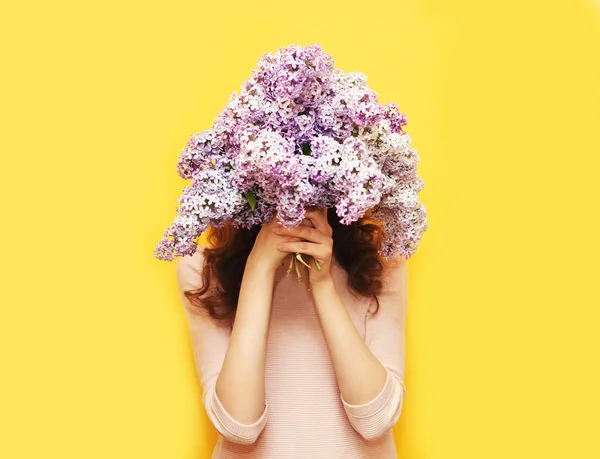 Mulher escondendo cabeça em flores lilás buquê sobre backgroun amarelo — Fotografia de Stock