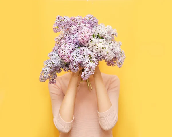 Mulher escondendo a cabeça em flores lilás bouquet sobre backg amarelo — Fotografia de Stock