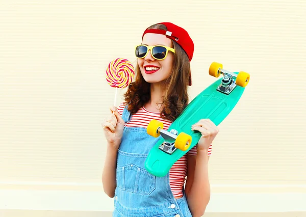 Porträt cooles lächelndes Mädchen mit Lutscher und Skateboard über dem Kopf — Stockfoto
