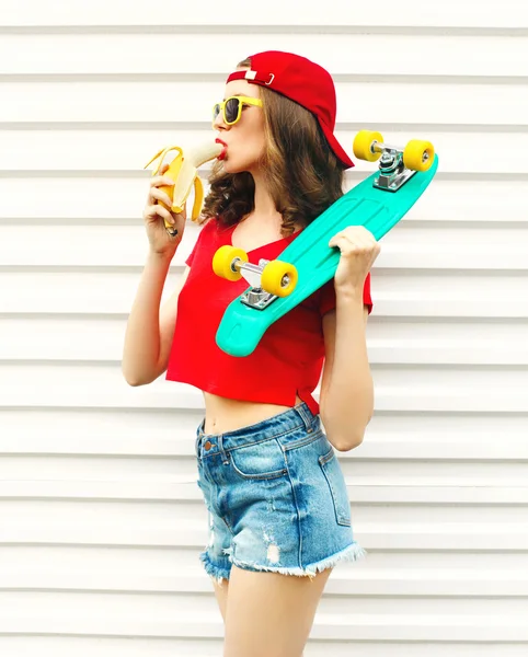 Mode vrij koel vrouw met skateboard eten van een banaan over w — Stockfoto