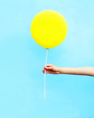 Sarı hava balonu mavi renkli arka plan üzerinde tutan el