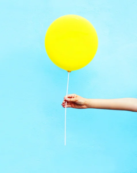 Hand som håller gula luftballong över färgglada blå bakgrund — Stockfoto