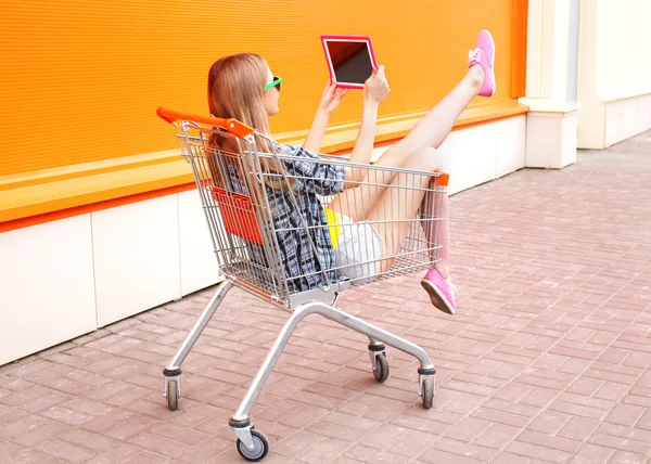 Beautiful young woman sitting in shopping trolley cart over colo — Stock Photo, Image