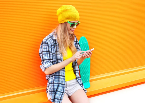 Moda bonita mujer usando smartphone con monopatín sobre color — Foto de Stock