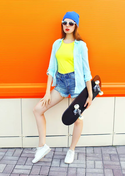 Mode mooi meisje met skateboard over kleurrijke oranje backgro — Stockfoto