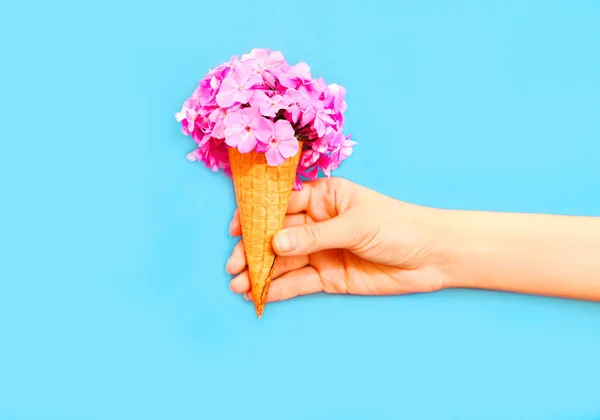 Mão segurando cone de sorvete com flores sobre fundo azul — Fotografia de Stock