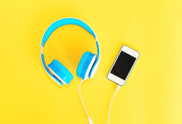 Hörlurar anslutna till vit smartphone över gul bakgrund — Stockfoto