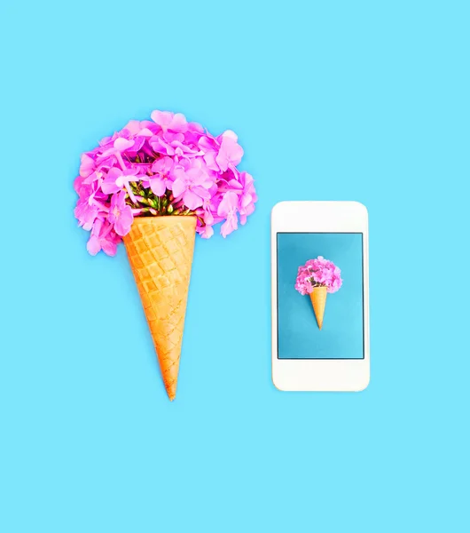 Cone de sorvete com flores e smartphone sobre azul ba colorido — Fotografia de Stock