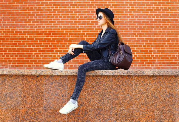 Модная молодая женщина в стиле чёрного рока, сидящая над бриком — стоковое фото