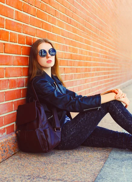 Fashion portrait woman in black rock style sitting over bricks w