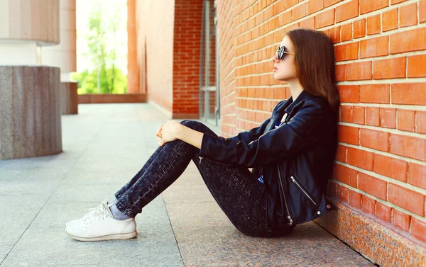 Mode kvinna i svart rock stil sitter över tegelstenar bakgrund — Stockfoto