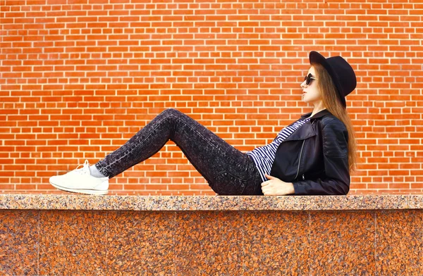 Moda joven mujer usando un estilo de rock negro acostado sobre ladrillos — Foto de Stock
