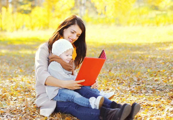 Счастливые улыбающиеся мать и ребенок сидит вместе глядя на книгу или — стоковое фото