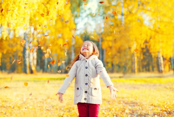 Menina feliz criança brincando se divertindo com folhas amarelas em — Fotografia de Stock