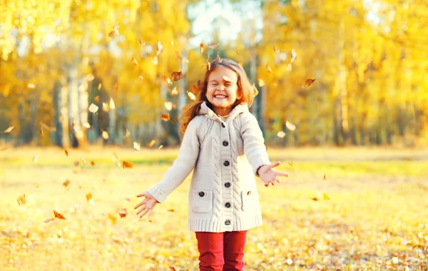 Menina feliz criança se divertindo brincando com folhas amarelas em — Fotografia de Stock