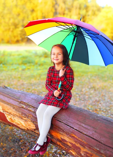 Happy Little Girl dziecko z kolorowym parasolem siedzi na drzewie i — Zdjęcie stockowe