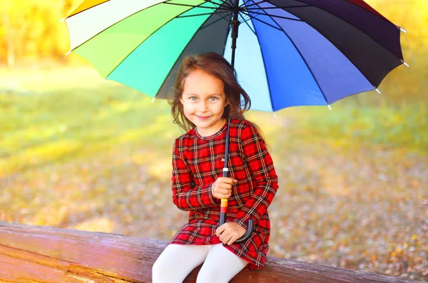 Portrait happy little girl child with colorful umbrella sitting — Stock Photo, Image