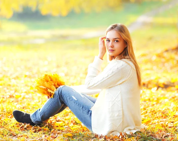 暖かいスーで黄色いカエデの葉で座っている美しい若い女性 — ストック写真