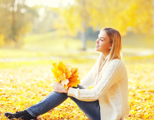 Belle jeune femme assise avec des feuilles d'érable jaune en su chaud — Photo