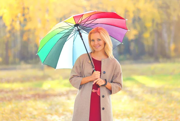 Schöne lächelnde Frau mit buntem Regenschirm in warmem sonnigem — Stockfoto