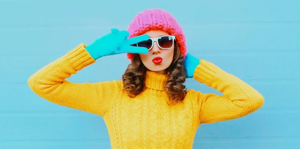 美しいです女性吹いて赤い唇甘いです空気キス身に着けている黄色ニットセーター ピンク帽子上の青の背景 — ストック写真
