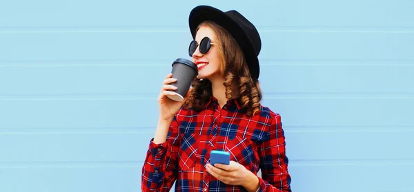 若いです女性飲料コーヒーの肖像電話を身に着けています黒丸帽子以上青の背景 — ストック写真