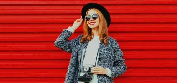 赤の背景に黒い丸帽子をかぶったヴィンテージフィルムカメラを持つ若い女性写真家 — ストック写真
