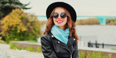 Şehirde siyah yuvarlak şapkalı, ceketli, güneş gözlüklü güzel bir genç kadının portresi.