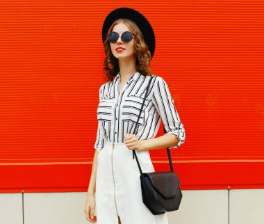 Güzel bir kadının portresi beyaz çizgili gömlek, siyah el çantası debriyaj, yuvarlak şapka, kırmızı arka plan