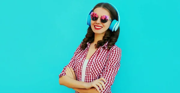 カラフルな青の背景の上にピンクのサングラスを身に着けている音楽を聞いて無線ヘッドフォンで笑顔の若い女性の肖像画のクローズアップ — ストック写真