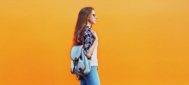 Sırt çantalı genç bir kadın turuncu bir arka planda yürüyor.