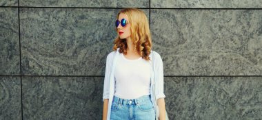 Avrupalı genç bir kadın gri duvar arkasından şehir caddesine bakıyor.