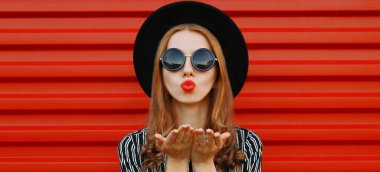 Kırmızı dudak üfleyen çekici bir kadının portresi. Kırmızı duvar arkasından tatlı bir öpücük yolluyor.