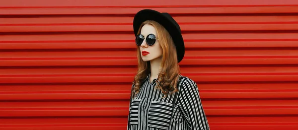 若い女性モデルの肖像画黒の白い縞模様のシャツを着て 赤い壁の背景に丸い帽子 — ストック写真