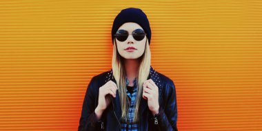 Portakal rengi arka planda siyah rock tarzında şık sarışın kadın portresi.