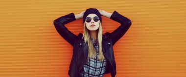 Portakal rengi arka planda siyah rock tarzında şık sarışın kadın portresi.