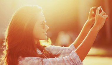 Güzel bir kadının portresi. Güneşli yaz akşamlarında telefonla selfie çekiyor.
