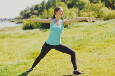Spor salonundaki kadın yaz parkında çimenler üzerinde egzersiz yapıyor.