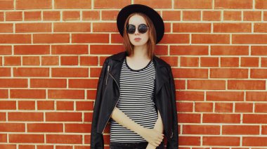 Duvarın arkasında siyah bir rock tarzı giyinmiş şık bir genç kadın modeli portresi.