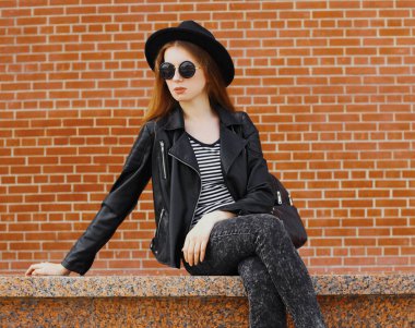 Duvarın arkasında siyah bir rock tarzı giyinmiş şık bir genç kadın modeli portresi.