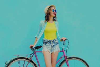 Mavi arka planda bisikleti olan mutlu, genç bir kadın.